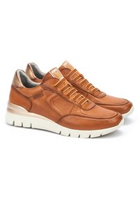 Zapatillas de cuero marrón con punta redondeada, cuello acolchado, suela de goma blanca y un sistema de cordones prominente. Acentuadas con detalles metálicos.