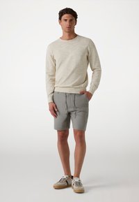 Light beige sweater with textured knit, paired with gray shorts featuring a drawstring waist. Model wears neutral-toned sneakers.