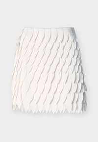 Jupe blanche avec des pièces de tissu superposées en forme de pétales créant un motif texturé de type écailles sur un fond uni.