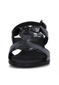 Sandali in vernice nera con più cinturini incrociati, accentuazione circolare, design open toe e suola in gomma nera. Cinturino alla caviglia regolabile.