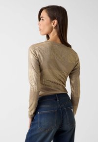 Glanzend, goudkleurig metallic top met lange mouwen, geribbelde textuur en horizontale lijnen, gecombineerd met donkerblauwe denim jeans met achterzakken.