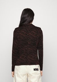 Långärmad topp i mörkbrunt med svart tigerrandmönster. Figursydd design med en mjuk textur och slagkrage.