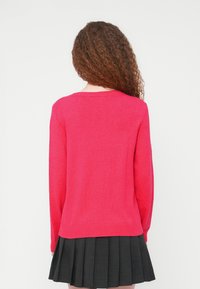 Πλεκτό πο υλόβερ φούξια με στρογγυλή λαιμόκοψη και μακριά μανίκια, με ριμπ τελείωμα και μανσέτες, συνδυασμένο με μαύρη φούστα με πιέτες.