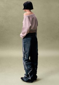 Sivá mikina s výstrihom z ramien spojená s tmavými širokými džínami z denimu so vzormi hviezd a otrepanými okrajmi, nosená s čiernymi topánkami.