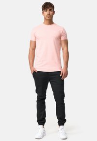 Svijetloružičasta majica kratkih rukava s okruglim izrezom, uparena s crnim tapered jogger hlačama. Bijeli tenisice upotpunjuju odjevnu kombinaciju. Nema vidljivih uzoraka.