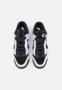 Black and white sports shoes with mesh panels, round laces, reinforced toe boxes, padded collars, and contrasting stitching details.