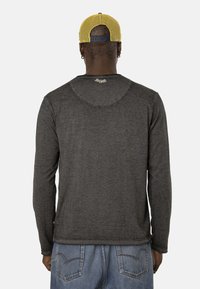 Chemise grise à manches longues avec un col rond et une texture lisse, affichée de dos. Accompagnée d'une casquette en mailles jaunes.