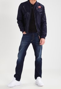 Marinblå bomberjacka med dragkedja fram, sidofickor och ett märke. Mörkblå jeans med slim fit och lätt blekning, matchat med vita sneakers.