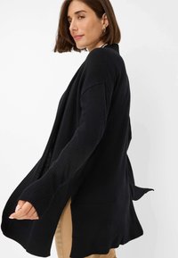 Schwarze Strickjacke mit lockerer Passform, gerippten Bündchen und seitlichen Schlitzen. Weiche Textur mit fließendem Design für optimalen Komfort.