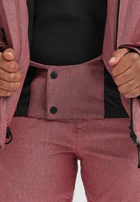 Rode en zwarte sportieve jas en broek, met een textuurstof, drukkersluiting en verstelbare trekkoorddetails.
