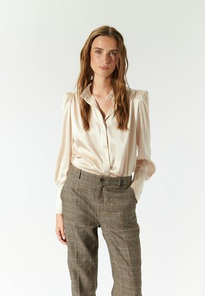 Satincreme Bluse mit einem Kragen und puffigen Ärmeln, kombiniert mit karierter, taillierter Hose in erdigen Tönen, die über einen Knopfverschluss verfügt.