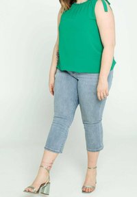 Top verde senza maniche con scollatura arricciata, abbinato a jeans cropped azzurri e sandali con tacco a blocco argento.
