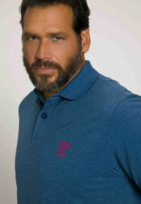 Polo homme en tissu tricoté bleu, avec un col et une patte de boutonnage à trois boutons. Logo brodé rose sur la poitrine. Texture lisse.