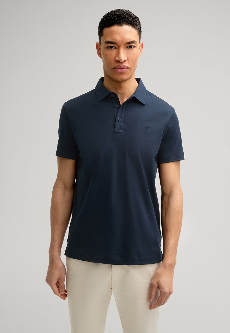 Polo de color azul oscuro, confeccionado en tejido suave, con cuello tipo polo, mangas cortas y un sutil logo bordado en el pecho.