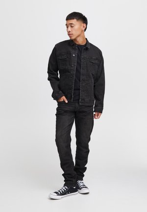 Giacca di jeans nera con bottoni, due tasche sul petto; abbinata a jeans skinny neri e sneakers nere con suola bianca. Look semplice e casual.