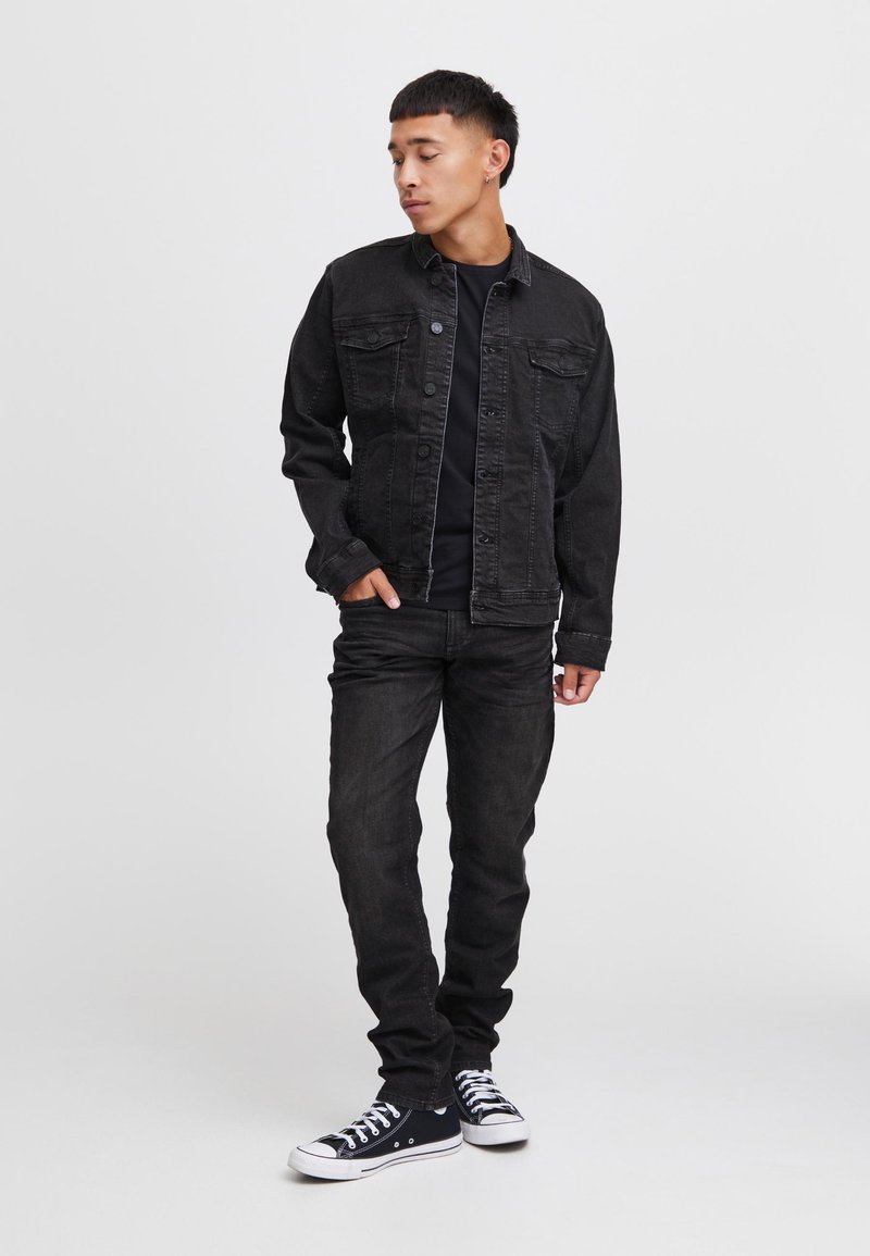 Czarna dżinsowa kurtka na guziki, z dwoma kieszeniami na piersi; w zestawie z czarnymi obcisłymi dżinsami i czarnymi sneakersami z białymi podeszwami. Prosty, casualowy wygląd.
