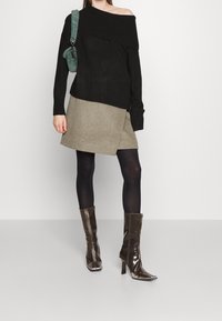 Svart avlastad tröja, grå omslagsskjorta, svarta strumpbyxor och glänsande bruna klackstövlar. Grön furu väska som accent.