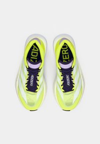 Zapatillas de running de color amarillo brillante con una parte superior de malla, detalles en púrpura y rayas blancas. Presentan una suela acolchada y cordones para un ajuste seguro.