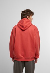 Oversized hooded sweatshirt in coral color, made of soft cotton blend, featuring a kangaroo pocket and ribbed cuffs and hem.