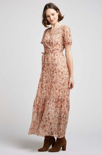 Robe maxi florale en pêche avec des manches courtes bouffantes, un design croisé et un ourlet à volants. Présente une taille ceinturée et des motifs complexes dans des tons d'orange.