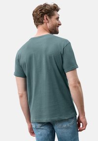 T-shirt in cotone verde con collo rotondo e maniche corte, caratterizzato da una sottile texture e una vestibilità rilassata, indossato con jeans blu.