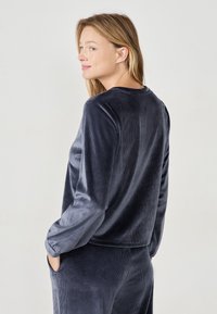 Top in corda di colore blu navy con maniche lunghe e scollatura rotonda. Texture morbida, vestibilità casual e dettaglio con tasca sul lato.
