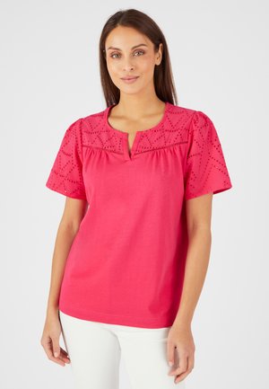 Roze katoenen t-shirt met korte pofmouwen, voorzien van geborduurde details en een notch halslijn. Gedirigeerd met witte broek.