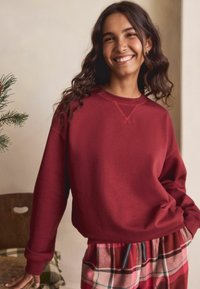 Viininpunainen collegepaita pyöreällä pääntiellä, resorit hihansuissa ja ompelukoristuksilla. Yhdistetty punavalkoisiin ruudullisiin housuihin.