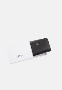 Portefeuille en cuir noir dans une boîte blanche, présentant une surface texturée et un logo doré. Design fermé avec une forme rectangulaire élégante.