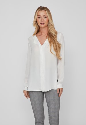 White long-sleeve blouse with a V-neckline and front button closure. Lightweight, semi-sheer fabric. Paired with gray plaid trousers.