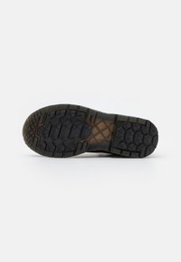 Suela de zapato de goma negra con un patrón texturizado, que presenta bandas únicas para un mejor agarre. La sección del tacón incluye un área transparente.
