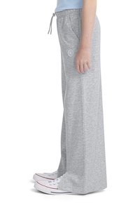 Γκρι φόρμες με χαλαρή εφαρμογή, κορδόνι στη μέση και λογότυπο. Φορεμένες με λευκά αθλητικά παπούτσια, αναδεικνύοντας μία χαλαρή αθλητική στυλιστική επιλογή.