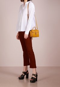 Biała koszula na guziki, brązowe spodnie z sztruksu, czarne sandały na platformie z ćwiekami oraz mała żółta torebka na pasku. Prosty design, jednolite kolory.