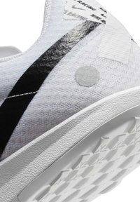 Baskets blanches avec tige en tissu texturé, bande noire, détail circulaire argenté et semelle extérieure en caoutchouc à motifs. Détails réfléchissants sur la tige.