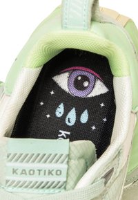 Interno di sneaker verde chiaro con soletta nera che presenta un design di occhio stampato, gocce d'acqua e il nome del marchio "KAOTIKO" in bianco.