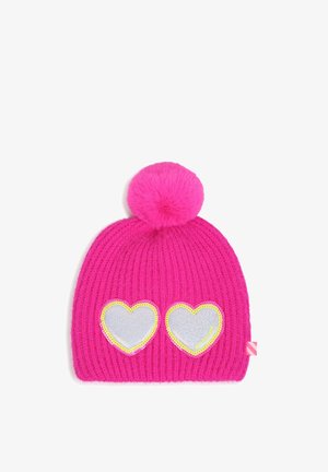 Felroze gebreide muts met een grote pompon bovenop en twee zilveren hartpatches omlijst met gele pailletten aan de voorkant.