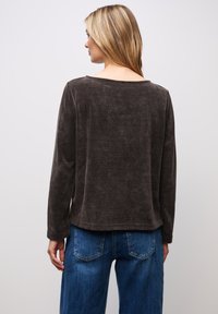 Top lungo a maniche lunghe di colore marrone con una scollatura ampia, caratterizzato da una vestibilità ampia e un orlo dritto, abbinato a jeans in denim blu.