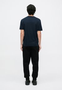 Tengerészkék rövid ujjú póló kerek nyakkal, fekete melegítőnadrággal és fekete cipővel párosítva, hátulnézetből egyszerű háttér előtt.