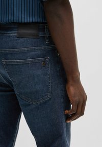 Mörkblå denimjeans med slim fit, med en läderpatch vid midjan och en fickdetalj med en liten metallaccent.