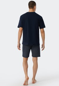 Camiseta de algodón azul marino con cuello redondo, combinada con pantalones cortos estampados que presentan puntos blancos sobre un fondo oscuro, pies descalzos.