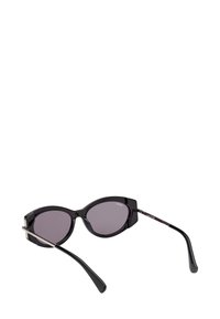 Černé sluneční brýle ve tvaru kočičích očí s tmavě zabarvenými skly a tenkými nožkami ležícími na bílé ploše.