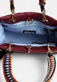 Bordeaux handtas met een glanzende afwerking, met een lichtblauwe binnenkant, gouden hardware en een gestructureerde, meerkleurige gevlochten schouderband.