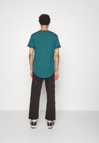 T-shirt azzurro a maniche corte con orlo arrotondato, abbinato a pantaloni in velluto a coste scuri e sneakers. Design semplice, texture liscia.