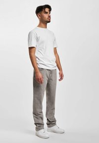Grijze jeans met een slim fit, gecombineerd met een eenvoudig wit t-shirt. Witte sneakers maken de look compleet. Eenvoudige achtergrond en neutrale kleuren.