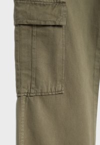 Gros plan d'un pantalon en tissu vert olive montrant une poche cargo rectangulaire avec rabat et coutures visibles.
