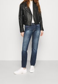 Černá kožená motorkářská bunda, na tělo; kombinovaná s modrými džíny s jemným opráním; doplněno bílými teniskami.