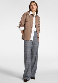 Bruine button-up shirt met geborduurde details, witte collshirt eronder en brede geruite broek in blauwe en grijze tinten. Fluwelen schoenen.