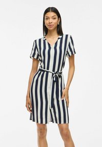 Abito a camicia con righe verticali blu marino e crema, maniche corte, scollo a V e cintura annodata in vita, caratterizzato da una texture di tessuto liscia.