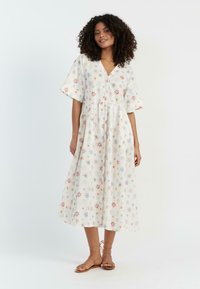 Witte katoenen jurk met bloemenpatronen in rood, blauw en groen. Heeft korte mouwen, een V-hals en een gelaagde rok. Leren sandalen.