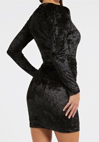 Robe bodycon en velours noir avec des manches longues, présentant un détail froncé sur le côté et une texture lisse et douce.
